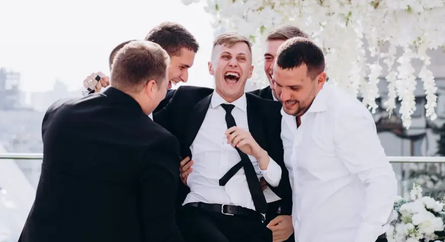 Śmiejący się pan młody otoczony przez przyjaciół. Świetne kawalerski pomysły na wspólne chwile przed ślubem.