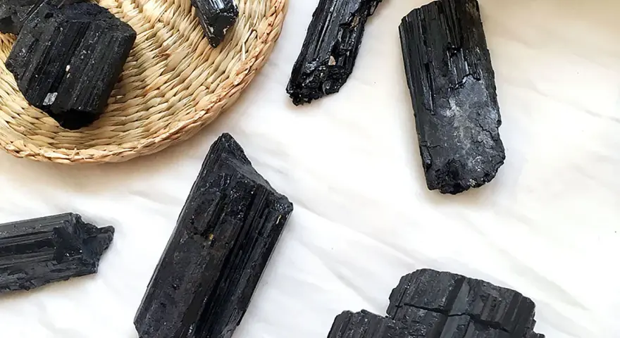 Cristales de turmalina negra, algunos en una cesta de mimbre, listos para atraer el amor y la protección.
