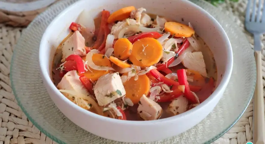 Pechuga de pollo en escabeche con zanahoria, pimiento rojo y cebolla, servida en un cuenco blanco sobre una base tejida.