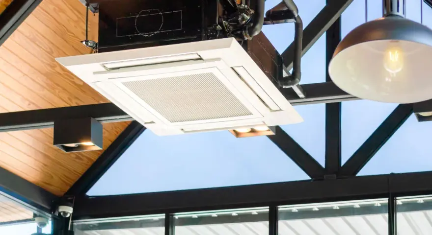 Unidad de cassette de un sistema VRV integrada en un techo de madera y metal, con luces y tuberías visibles.