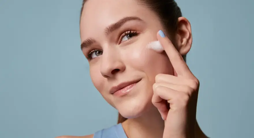 Donna applica schiuma sul viso, un gesto essenziale per la skincare routine mattina e sera. Pelle luminosa e curata.