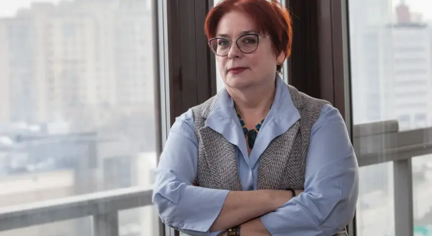 Kobieta w okularach, z rudymi włosami, opiera się o okno. Jej postawa sugeruje siłę i determinację w odpowiedzi na pytanie, jak żyć po rozwodzie.