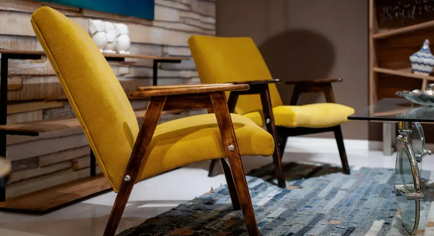 Due poltrone gialle con struttura in legno scuro, un tappeto patchwork e un tavolino in vetro. Un tocco di arredamento anni '70 italiano.