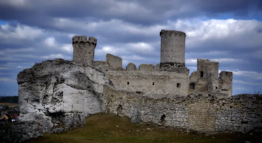 Ruiny zamku Ogrodzieniec na skale, z wieżami i murami, pod burzowym niebem. Idealne miejsce na trasę pełną historii.