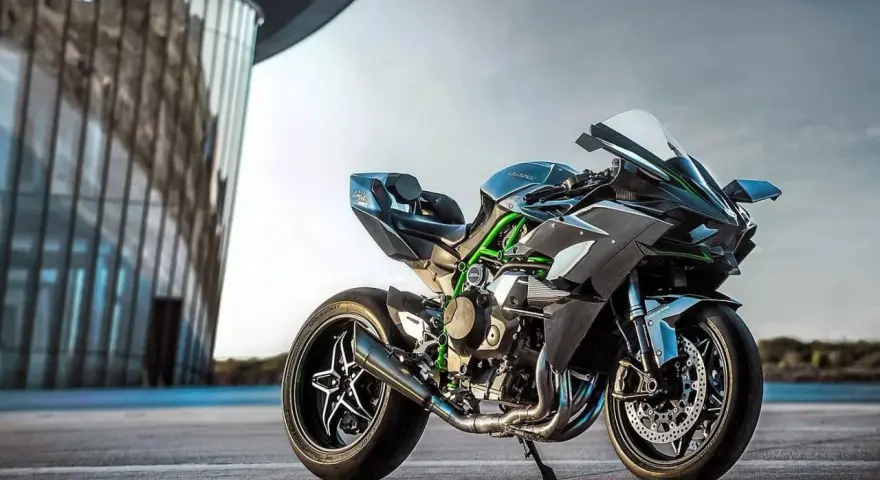 Kawasaki H2R – maszyna, która w mgnieniu oka osiąga 100 km/h. Czarny, sportowy motocykl z zielonymi akcentami na ramie, zaparkowany przed nowoczesnym budynkiem.