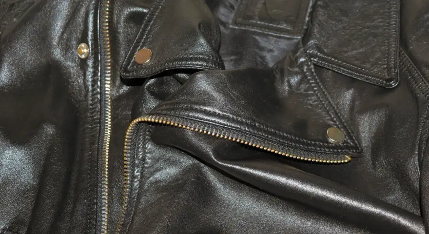 Dettaglio di una giacca in ecopelle nera con zip dorata e bottoni a pressione. Si pensa a come lavare giacca ecopelle in lavatrice.