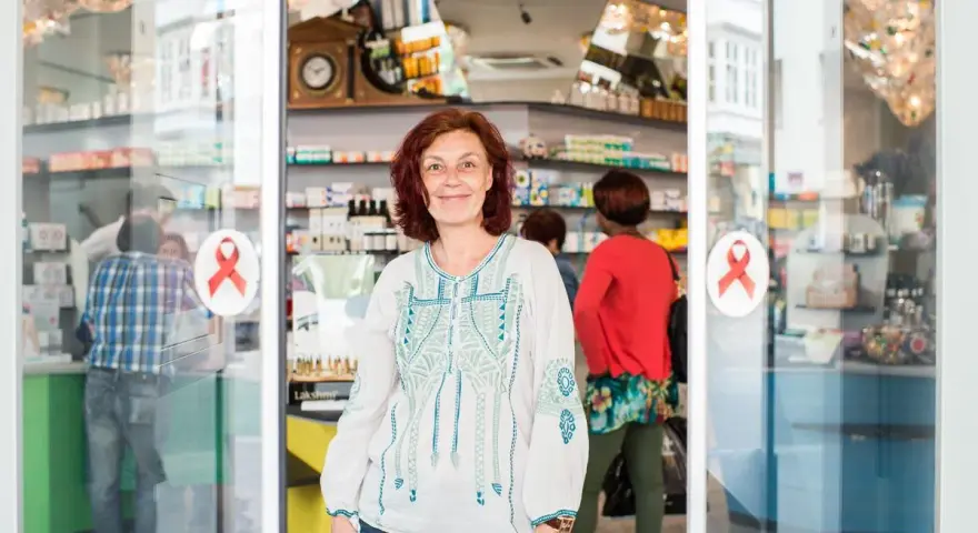 Frau lächelt vor einer Apotheke mit roten Aids-Schleifen am Eingang.
