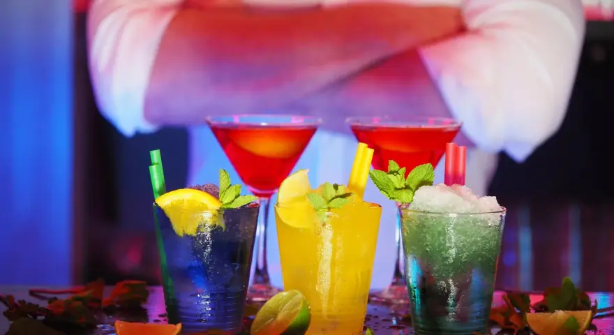 Kolorowe drinki z owocami i miętą na barze, w tle barman.