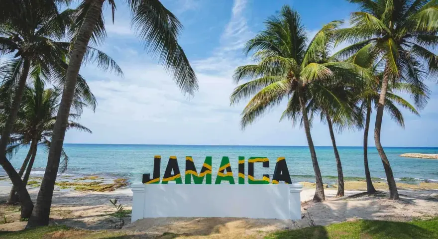 Napis "JAMAICA" na tle plaży, morza i palm.