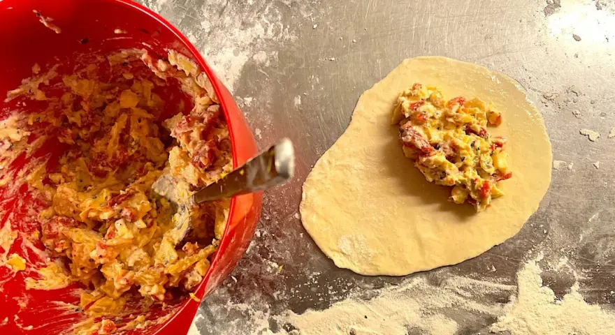 Fyllning till piroger recept läggs på deg. En röd skål med fyllning syns till vänster.