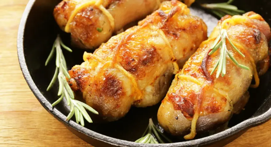 Involtini di pollo dorati e succulenti, legati con spago da cucina e guarniti con rametti di rosmarino, in una padella di ghisa.