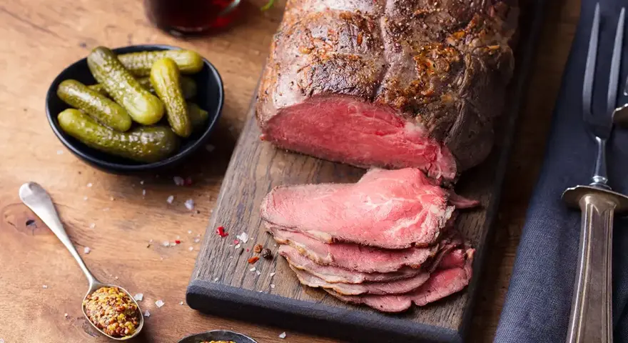 Un délicieux roti de boeuf, tranché et servi avec des cornichons, de la moutarde et une boisson foncée.
