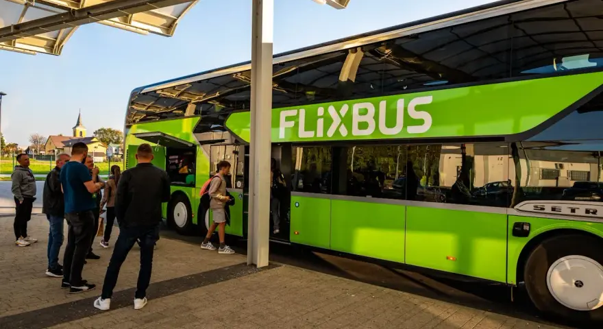 Zielony autobus FlixBus na przystanku, z pasażerami wsiadającymi i wysiadającymi.