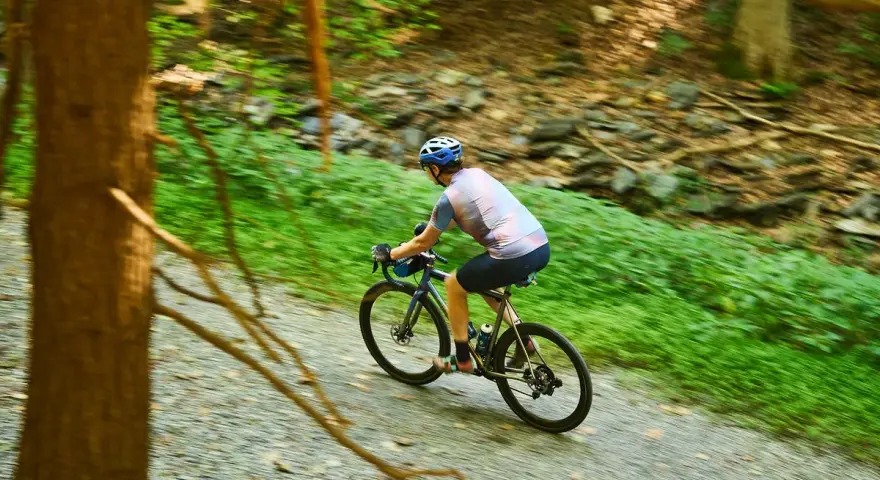 A cyclist enjoys biking 50 miles a week on a gravel path through a lush green forest.