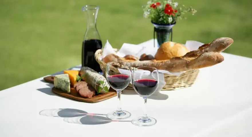 Dwa kieliszki pełne rubinowego pinot noir wina, obok deska serów, wędlin i kosz świeżego pieczywa.