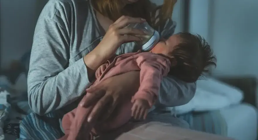 Mama karmi butelką niemowlę, które obudziło się w nocy z płaczem.