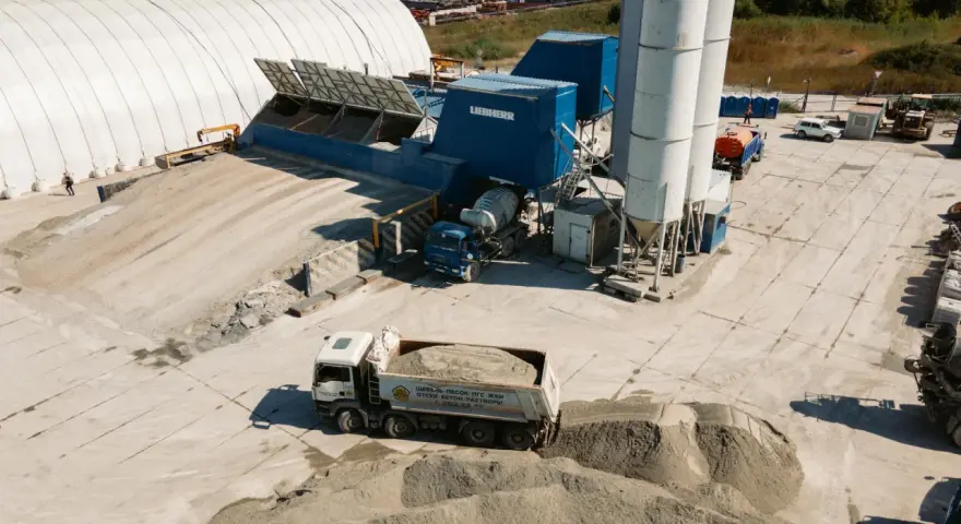 Beton skład z ciężarówką wyładowującą materiał. W tle silosy i budynki przemysłowe.