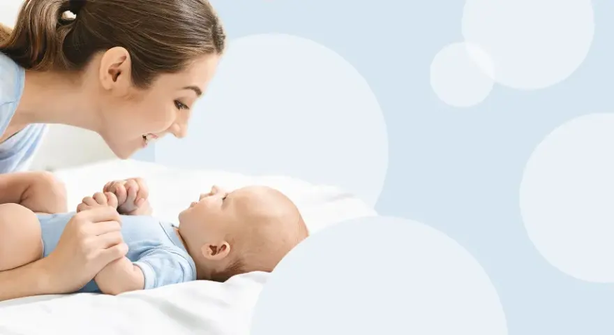 Uśmiechnięta mama pochyla się nad dzieckiem, które świadomie mówi "mama".
