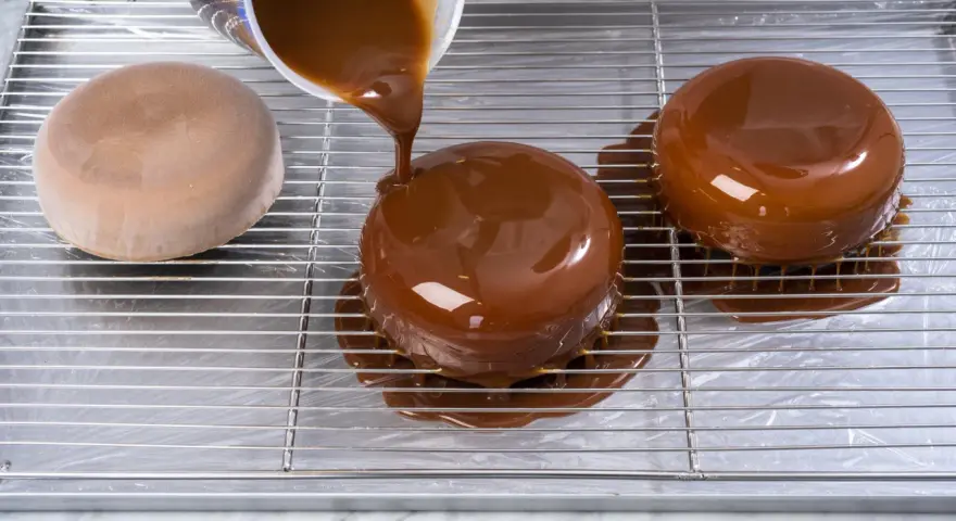Dolce lucido ricoperto da una colata di cioccolato. La glassa scende sui lati, creando un effetto invitante.