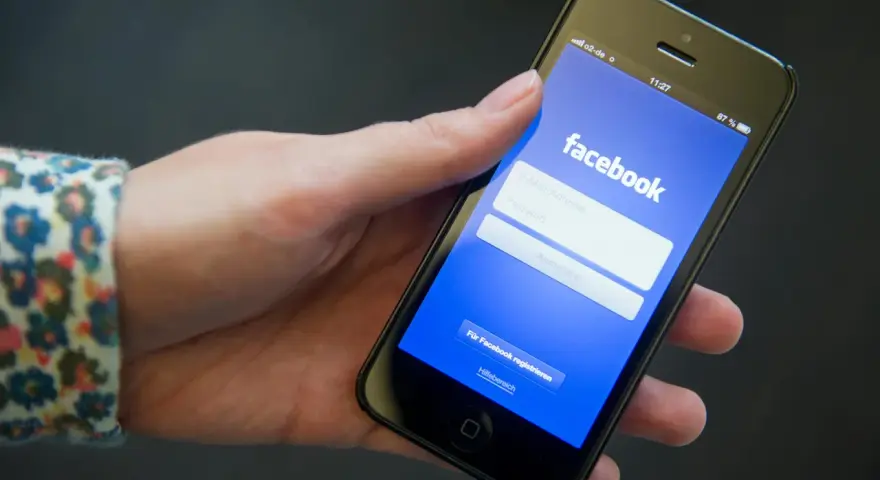 Eine Hand hält ein Smartphone mit der Facebook-Anmeldeseite.