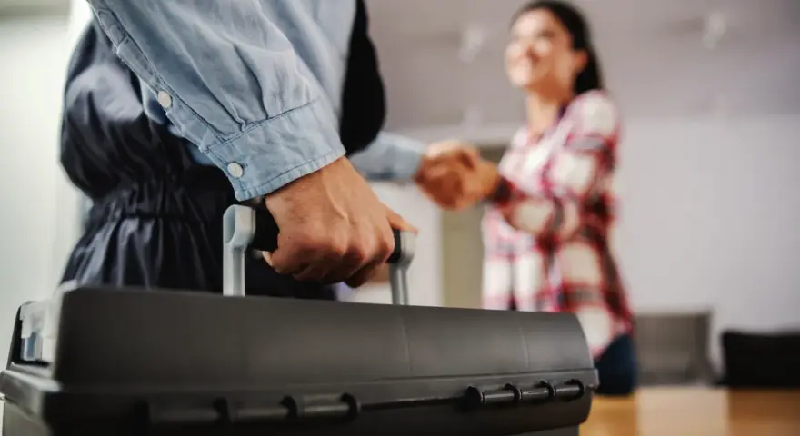 Un plombier arrive avec sa boîte à outils pour régler une fuite d'eau avant compteur sur terrain privé. Une cliente le remercie.