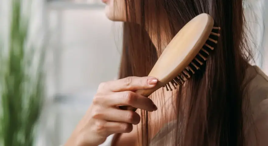 Eine Frau kämmt ihr langes, dunkles Haar mit einer Holzbürste. Sie achtet auf ihre Haare, um Haarausfall bei Frauen im Alter vorzubeugen.