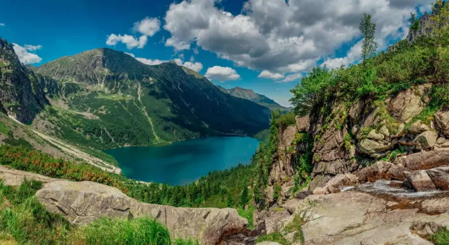 Majestatyczne tatry szczyty otaczają turkusowe Morskie Oko. Chmury na niebie dodają dramatyzmu krajobrazowi.