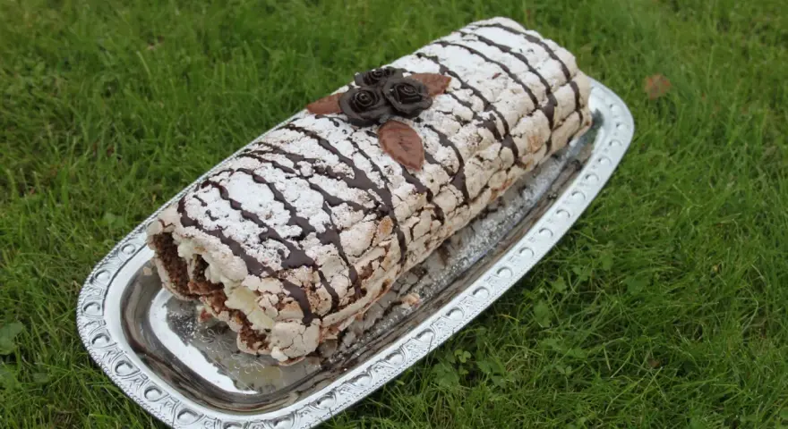 En läcker Budapestrulle med choklad och grädde, dekorerad med chokladrosor och pudersocker. Perfekt för ett sommarfika!