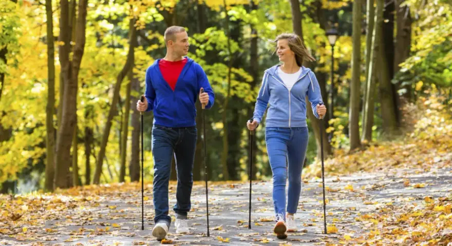 Para spaceruje po jesiennym parku, ciesząc się chodzeniem z kijkami.