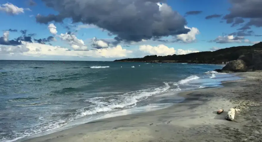 Onda che lambisce la spiaggia sabbiosa dell'Isola d'Elba, con il mare azzurro e nuvole scure nel cielo.