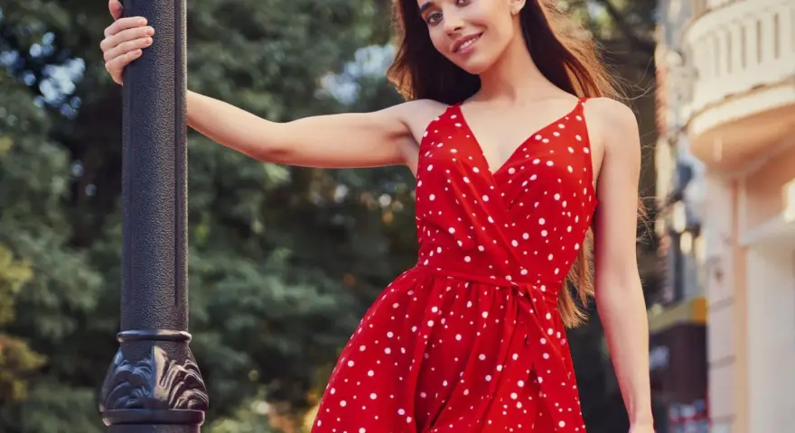 Junge Frau in einem roten Kleid mit Polka Dot Muster lehnt an einer Laterne.