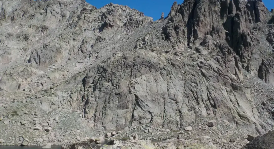 Vetta frastagliata di un monte rotondo, con rocce grigie e un lago alpino sullo sfondo.