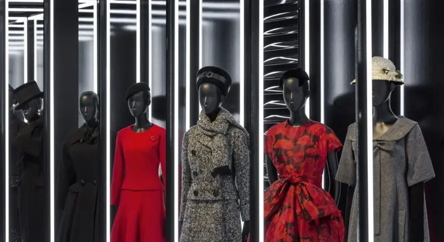 Manichini con abiti eleganti, un omaggio all'eleganza e all'origine Dior. Rossi, neri e grigi, con cappelli e sciarpe.