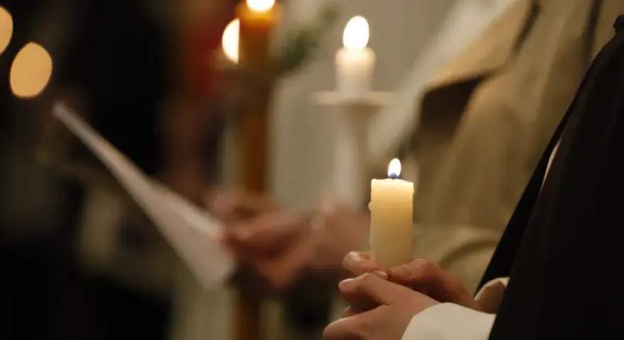 Dłonie trzymają płonące świece, symbolizujące poświęcenie ognia podczas uroczystości.