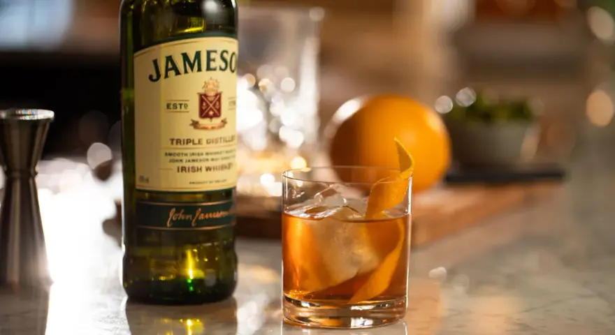 Old Fashioned na bourbonie czy na żytniej whisky? Jameson Irish Whiskey obok drinka z pomarańczą i lodem.