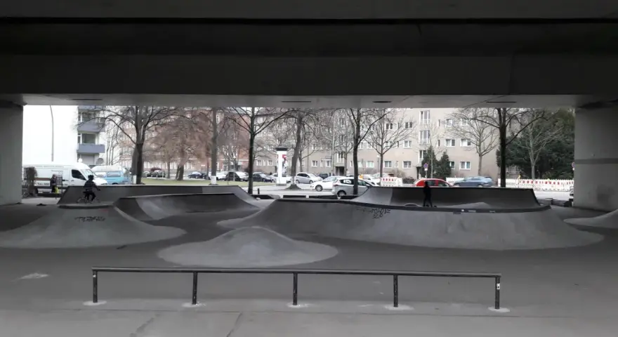 Ein leerer Berlin Skatepark unter einer Brücke. Ein Radfahrer fährt durch die Betonlandschaft.