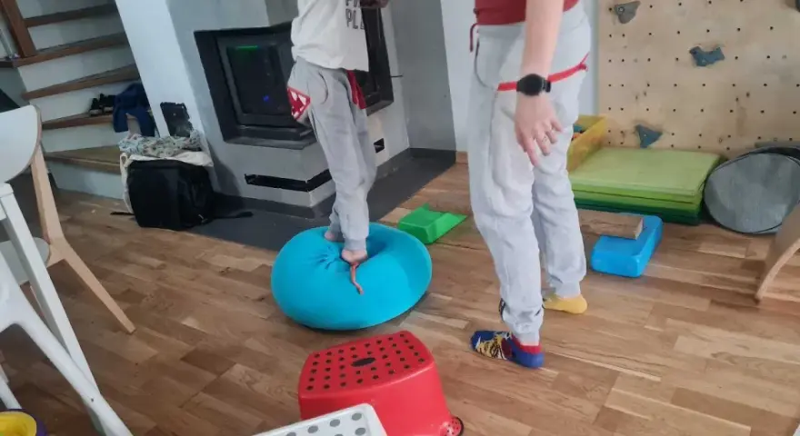 Dziecko ćwiczy równowagę na niebieskiej poduszce, część domowej ścieżki sensorycznej dla dzieci.