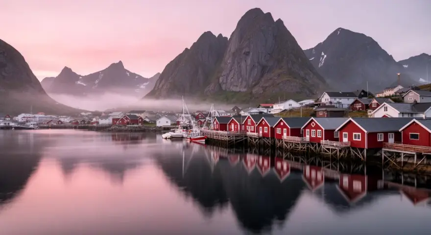 Röda fiskestugor vid vattnet i Lofoten, med berg och rosa himmel. En dröm om norrsken.