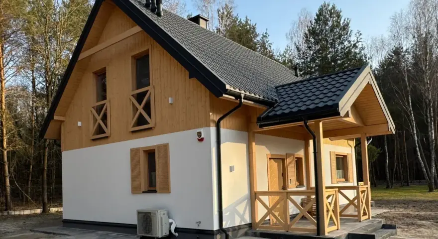 Nowy dom w lesie, drewniane elementy i biały tynk. Prowadzenie budowy domu zakończone sukcesem, gotowy do zamieszkania.