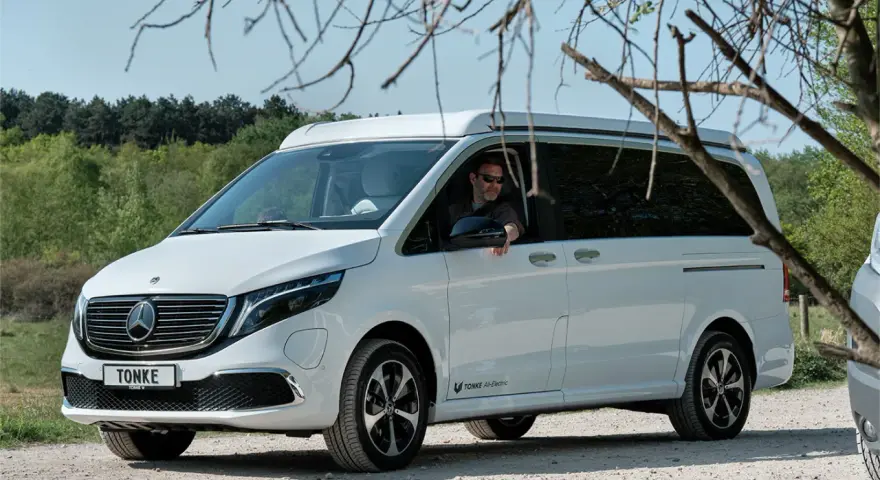 Vit eldriven husbil från Tonke parkerad på grusväg. En man med solglasögon sitter bakom ratten.