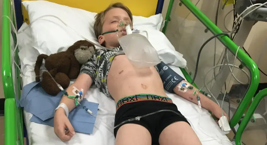 Chłopiec w szpitalnym łóżku z maską tlenową, podłączony do aparatury. To obraz walki z zapaleniem opon mózgowych u dzieci.
