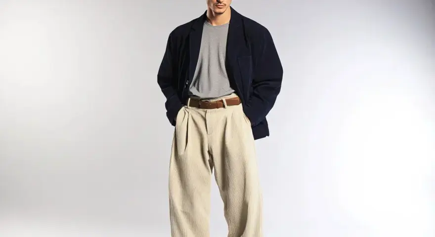 Uomo con spezzato giacca blu scuro, maglietta grigia e pantaloni beige a vita alta.