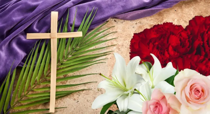 Cruz de palma, lirios blancos y rosas rosadas, con tela morada y flor de semana santa roja.
