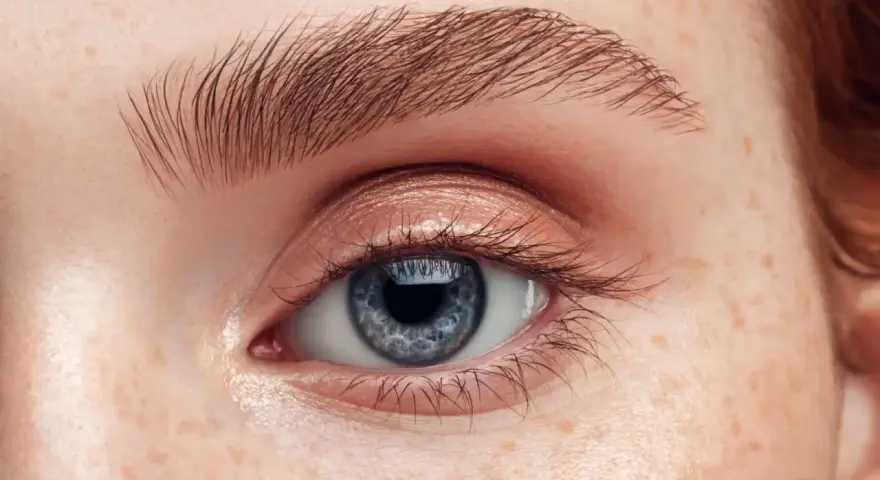 Nahaufnahme eines blauen Auges mit Sommersprossen und perfekt geformten Augenbrauen.