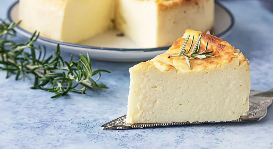 Una fetta di torta di ricotta soffice e dorata, guarnita con rosmarino, su un piatto da torta.