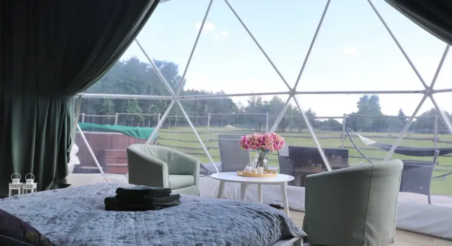 Wygodne łóżko i fotele w kopule z widokiem na zielone ranczo targówka.