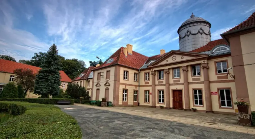 Pałac Maltzanów z charakterystyczną wieżą i czerwonym dachem, otoczony zielenią.