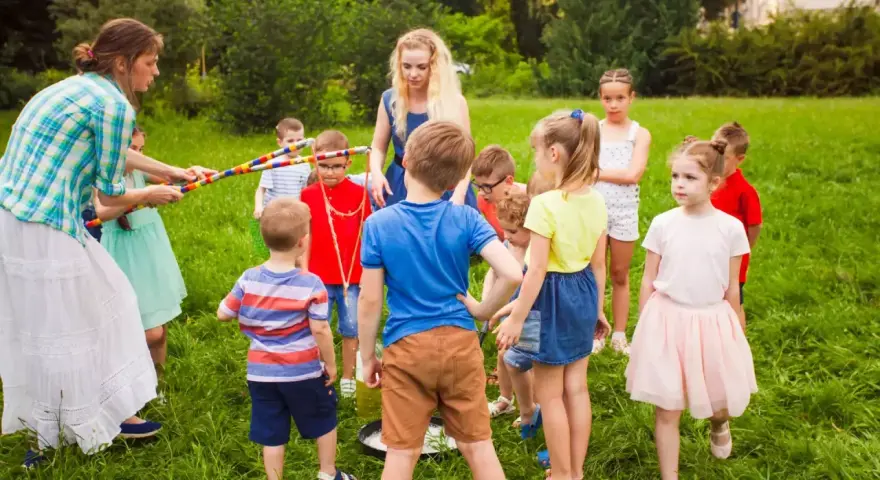 Des animateurs et des enfants jouent dehors dans l'herbe avec des cerceaux colorés.