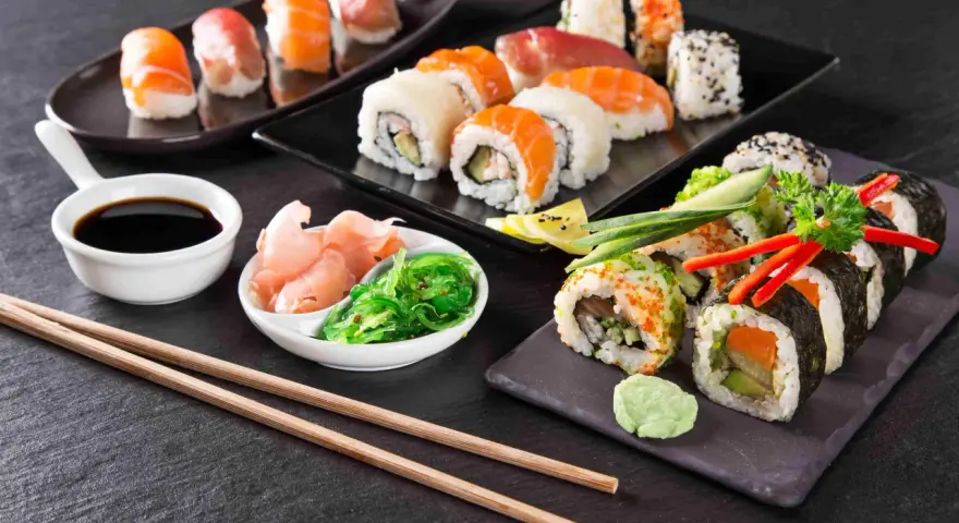 Pyszne sushi, w tym uramaki, z łososiem i awokado, podane z imbirem, wasabi i sosem sojowym.