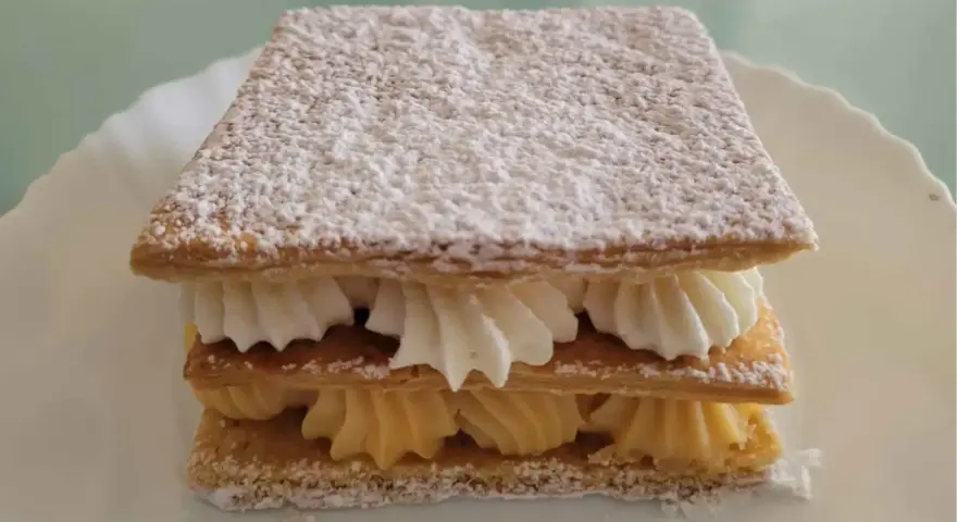 Delicioso milhojas de crema, con capas crujientes de hojaldre y rellenos de crema pastelera y nata montada, espolvoreado con azúcar glas.